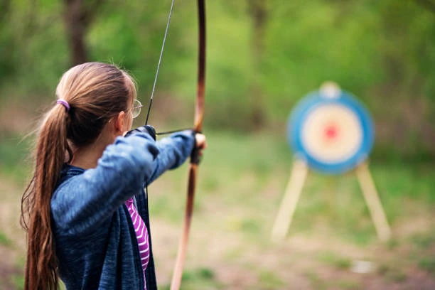 girl shooting bow at target in the forest